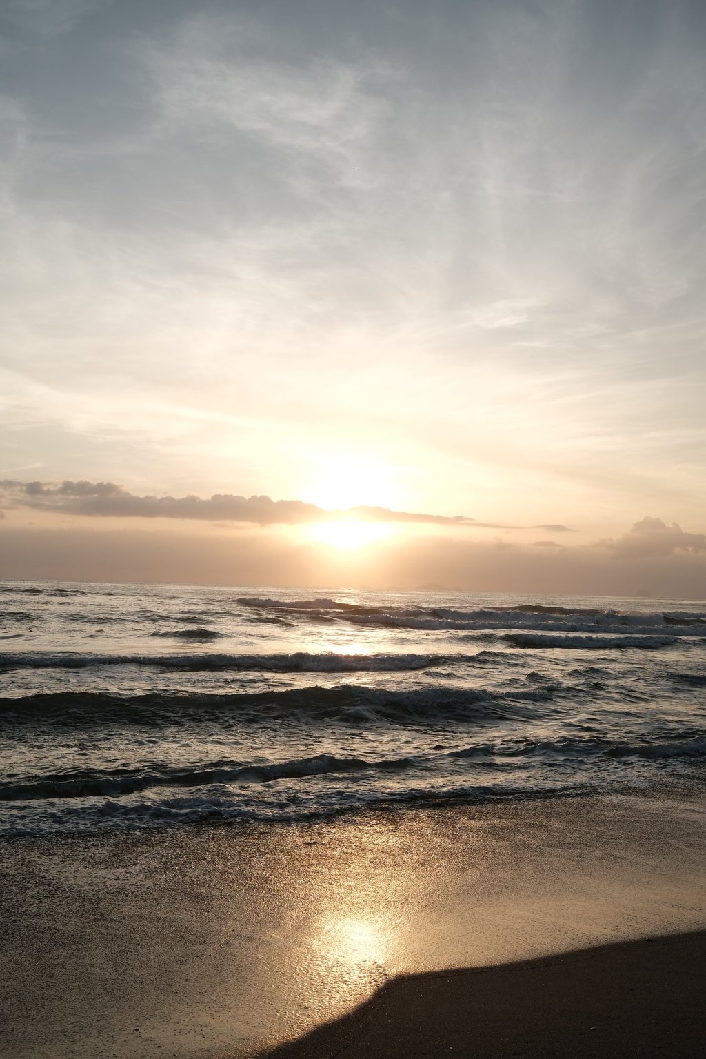 Golden sunrise over ocean waves on a sandy beach under a cloudy sky.