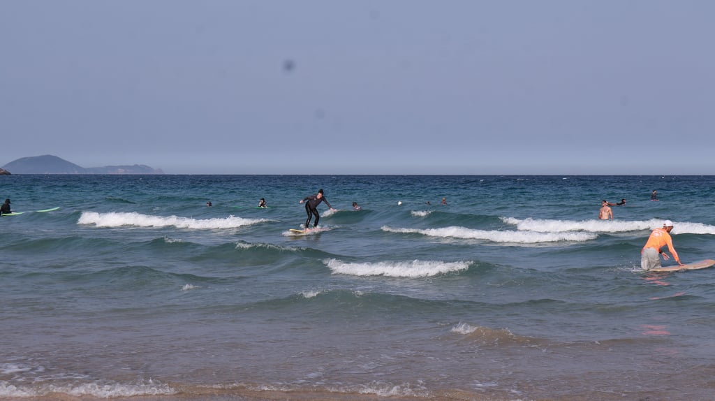 Surfers catching waves in the blue ocean water at a sandy beach on a clear day.