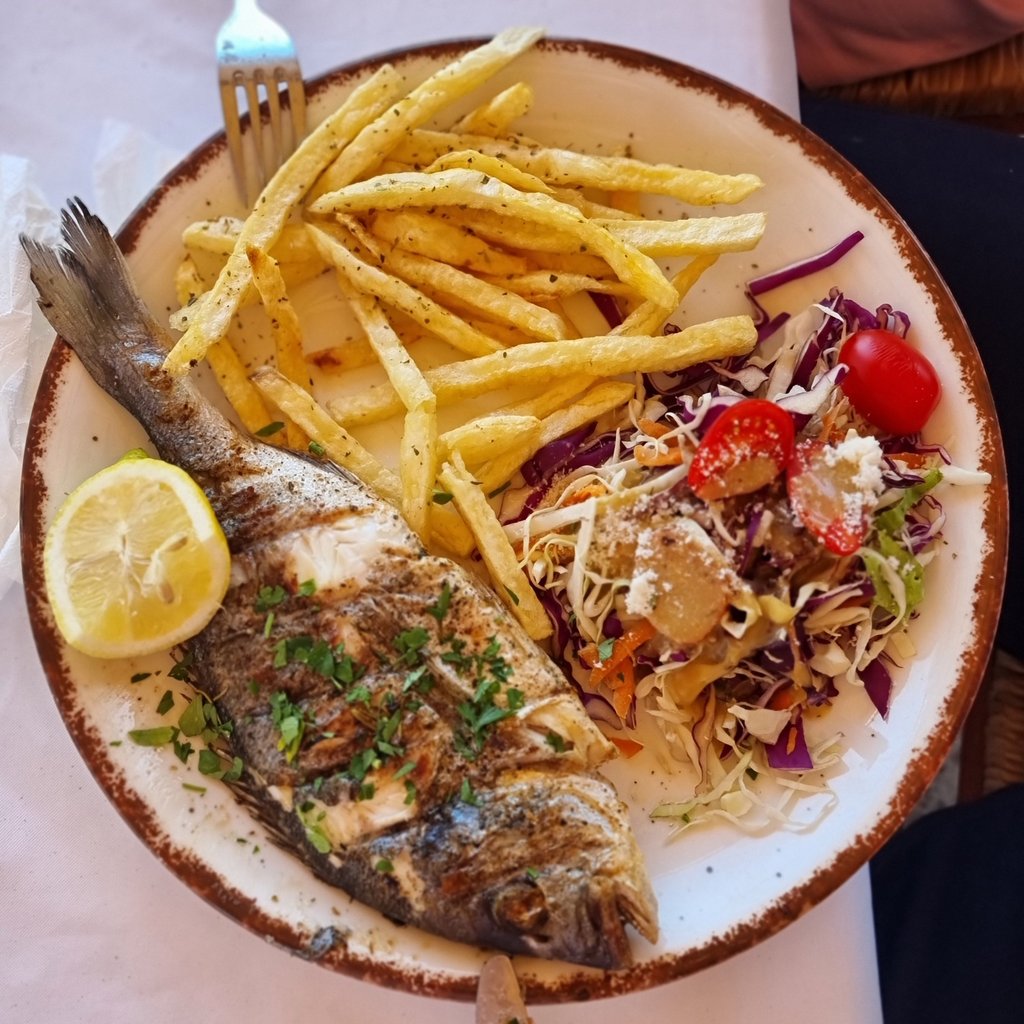 Grilled whole sea bream served with crispy french fries, fresh garden salad, and a lemon wedge.