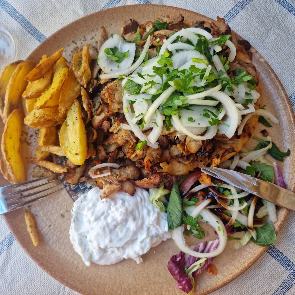 A plate of Greek chicken gyros with potato wedges, tzatziki sauce, and a fresh salad.