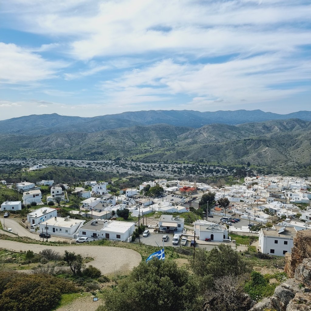 Panoramic view of white houses in a traditional Greek village nestled among rolling hills and mountains.