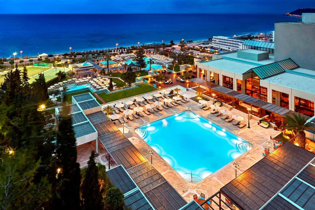 Luxury beach resort at dusk with illuminated swimming pools, tennis courts, and ocean views.