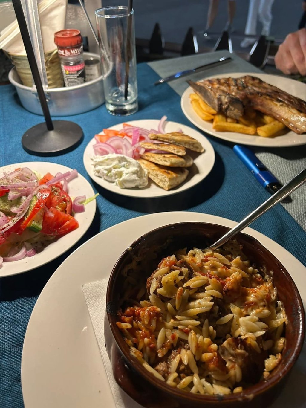 Authentic Greek dinner featuring beef giouvetsi with orzo pasta, fresh Greek salad, and pita bread with tzatziki.