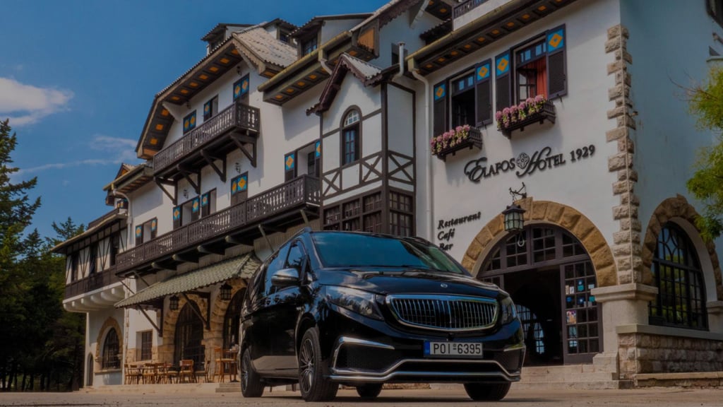 Luxury black Mercedes-Benz chauffeur van parked outside the historic Elafos Hotel in Rhodes, Greece.