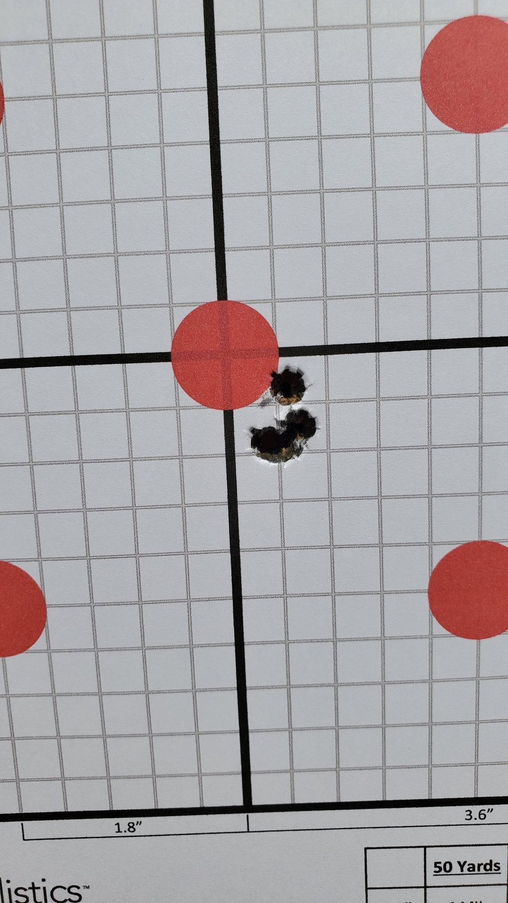 Close-up of a paper shooting target with a tight grouping of bullet holes near the red bullseye.