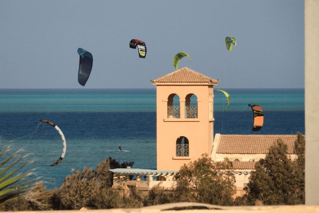 Kitesurfers flying colorful power kites over the blue ocean near a coastal villa tower in El Gouna..
