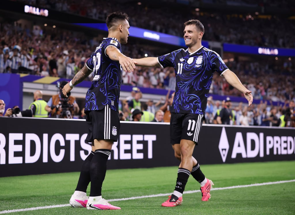 Argentina soccer players in black jerseys celebrate a goal on the field at a stadium.