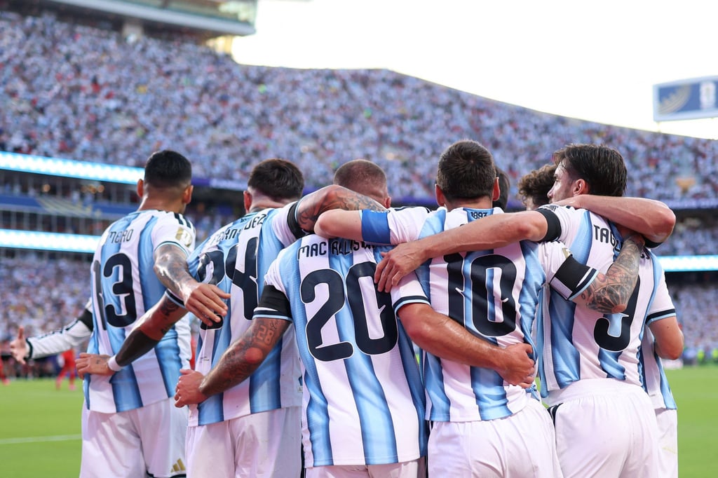 Argentina national football team players in blue and white jerseys huddle during a match in a packed stadium.