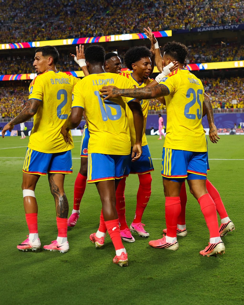 Colombia national football team players in yellow jerseys celebrating a goal on a stadium pitch.