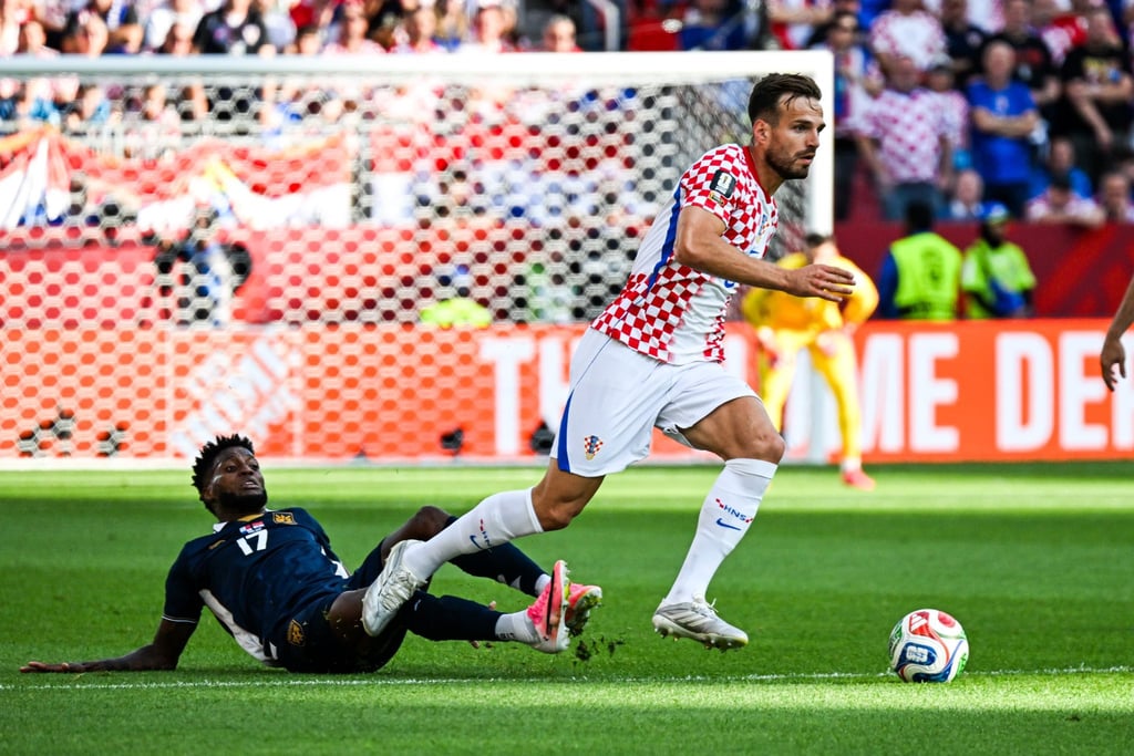 Croatia soccer player dribbles past a sliding defender during an intense international match.