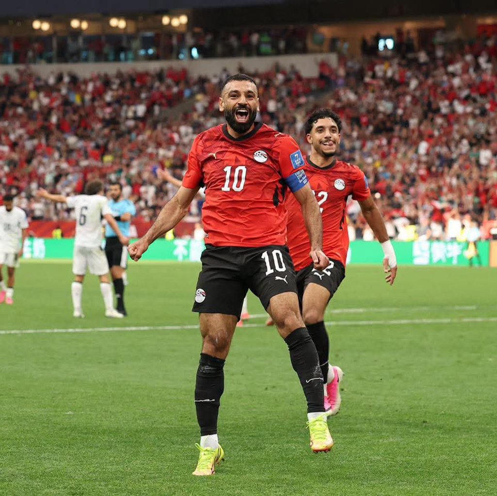 Egypt soccer player wearing a red jersey celebrates a goal on the field in a crowded stadium.