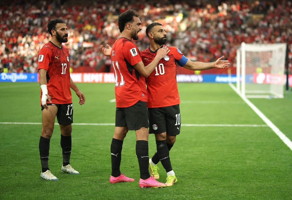 Egypt national football team players in red jerseys celebrating on a soccer field during a match.