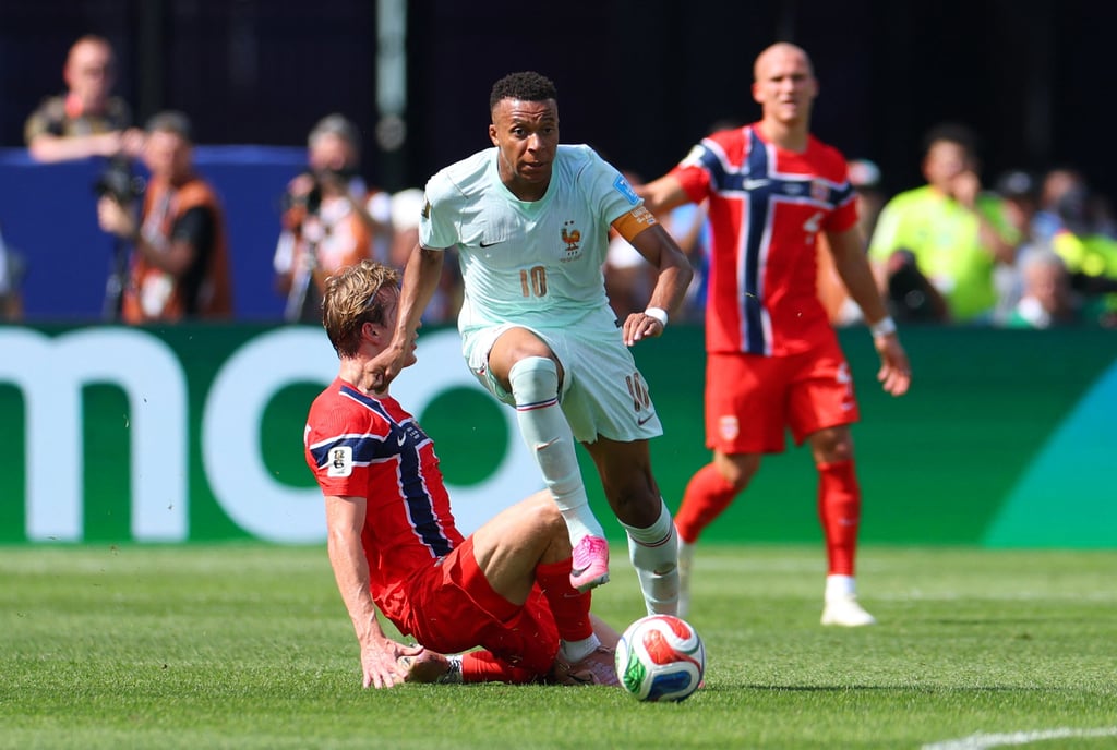 French soccer player dribbles past a sliding Norwegian defender during a competitive match.