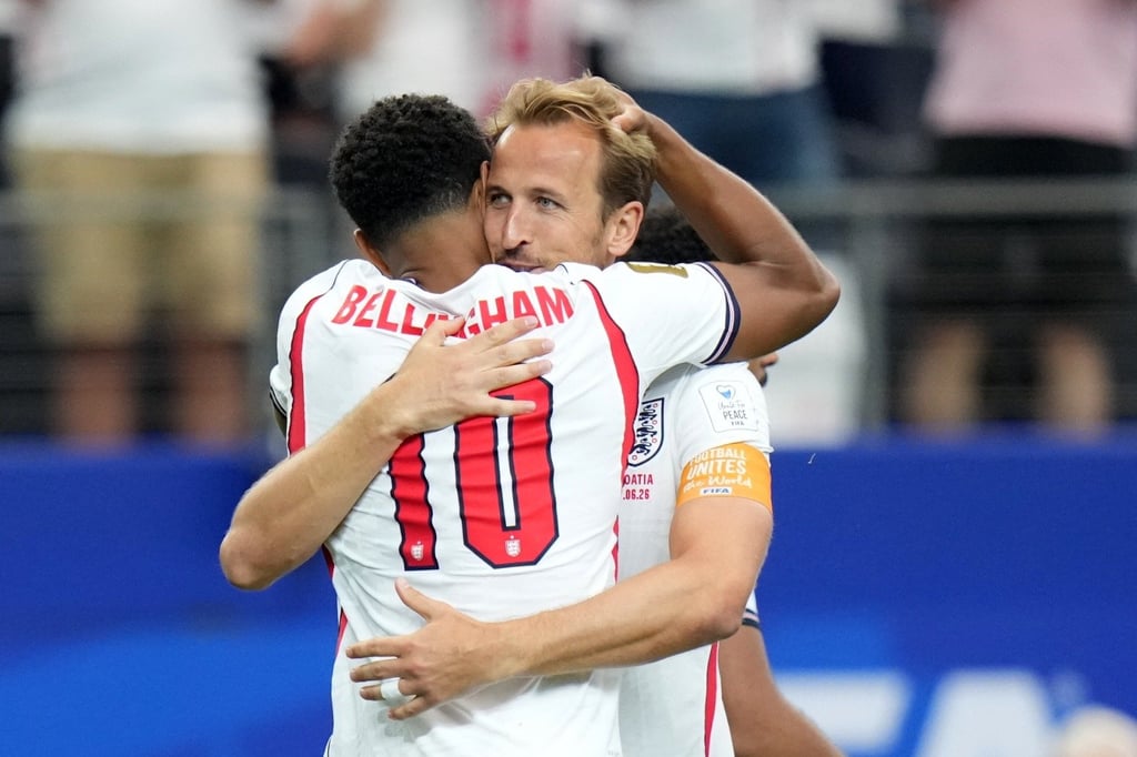 England football players Harry Kane and Jude Bellingham embrace during a match on the field.