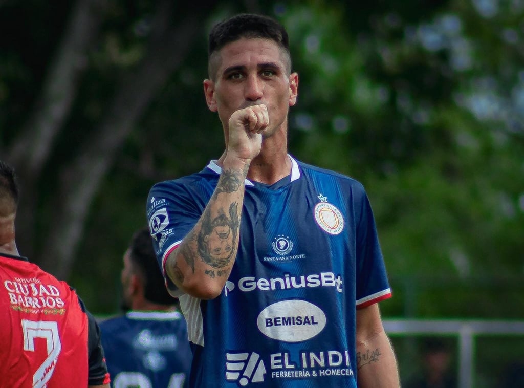 Professional soccer player in a blue jersey celebrating a goal with a kiss on his tattooed hand.