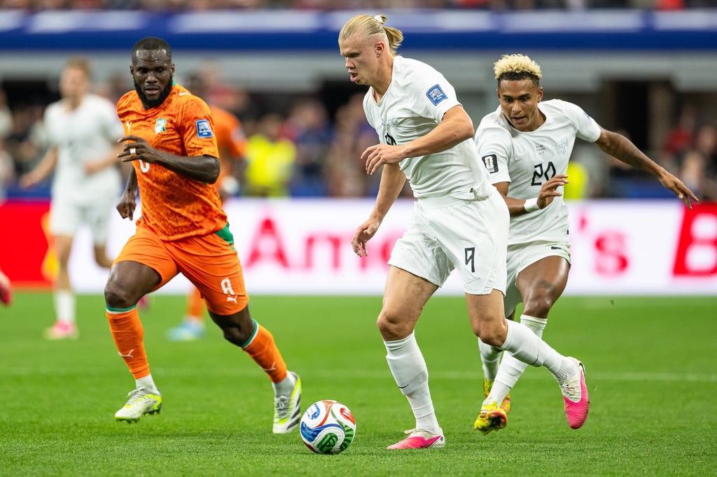 Erling Haaland dribbles a soccer ball past defenders during a high-action international match.