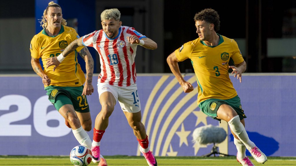 Paraguay and Australia national team players competing for the ball during a professional soccer match.