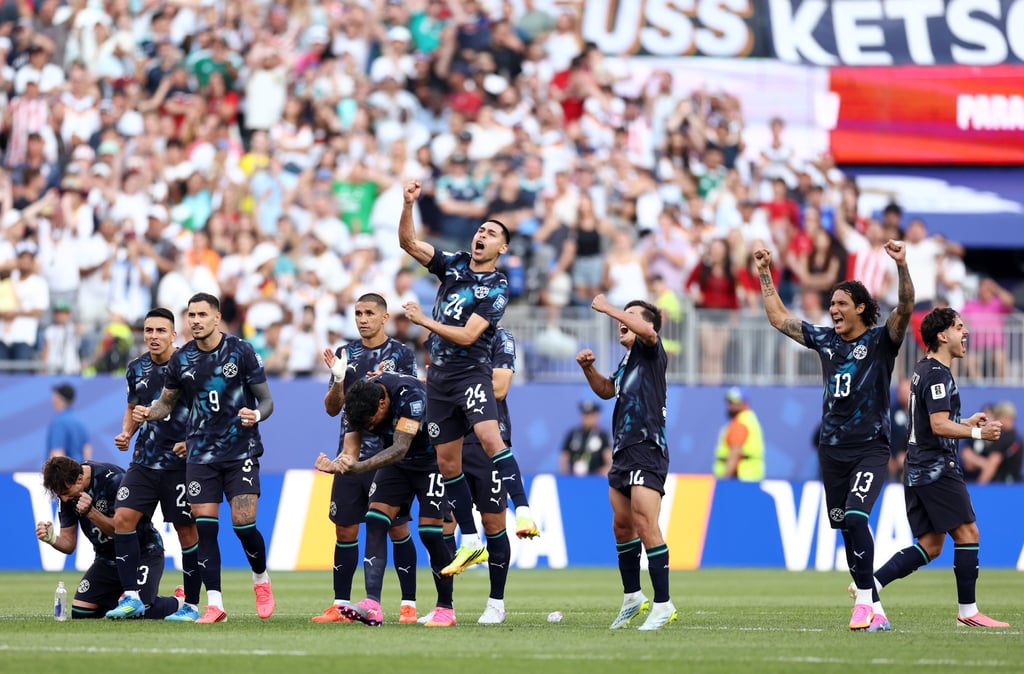 Professional soccer players in black jerseys celebrate a goal on the field in front of a crowded stadium.