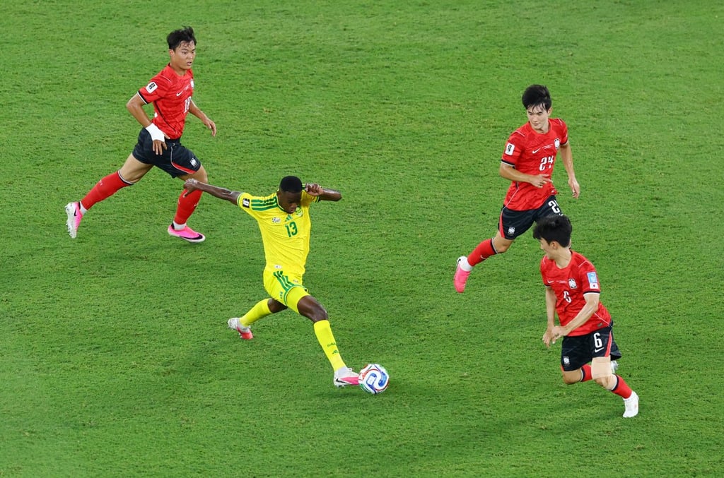 A soccer player in a yellow jersey dribbles past South Korean defenders on a green grass field.