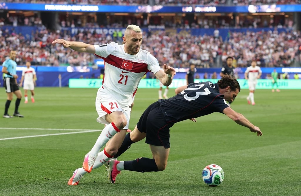 Turkey national football team player dribbles past a falling opponent during a competitive soccer match.