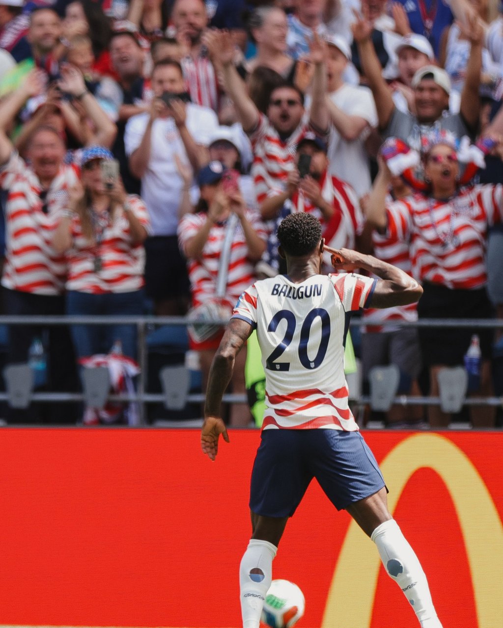 USMNT player Folarin Balogun celebrates a goal in front of cheering soccer fans in the stadium.