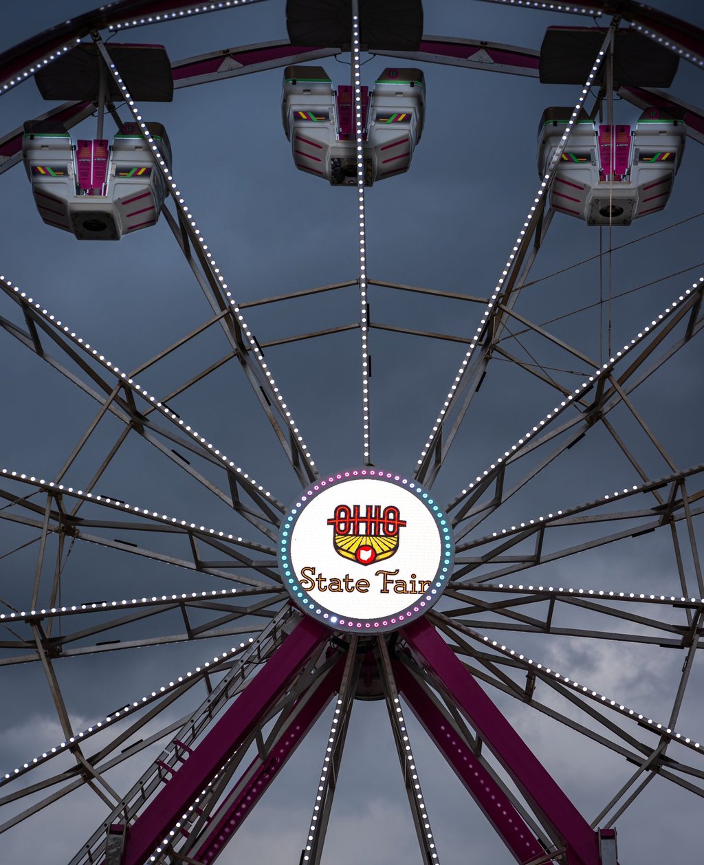 A Ferris wheel at the Ohio State Fair with illuminated passenger gondolas against a cloudy evening sky.