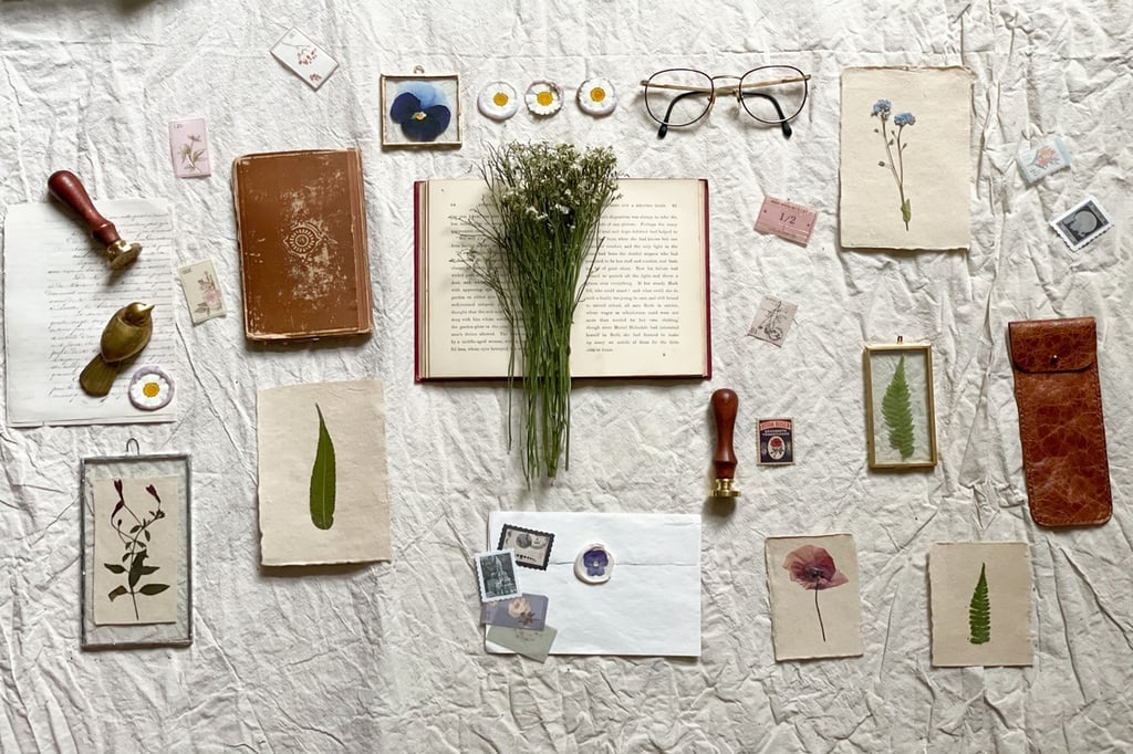 Vintage flat lay with dried flowers, old books, antique stamps, and glasses on a wrinkled white linen background.