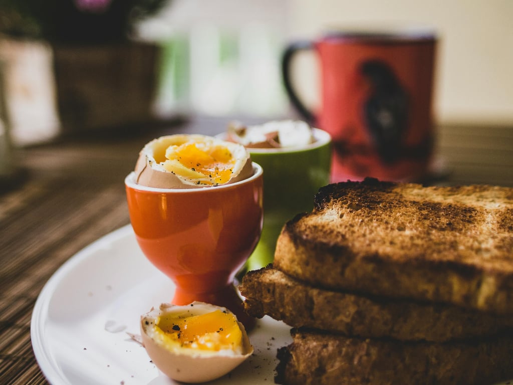Soft boiled egg in an orange egg cup with whole wheat toast soldiers on a breakfast plate.