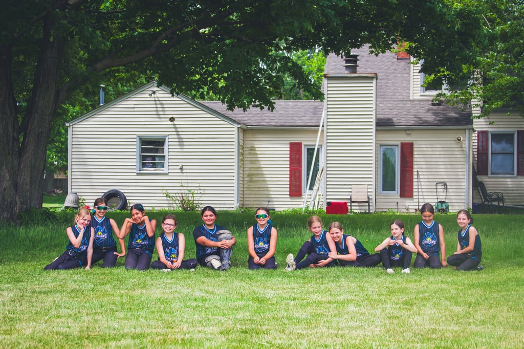 Photo of 10u Dragons sitting in grass in front of white house