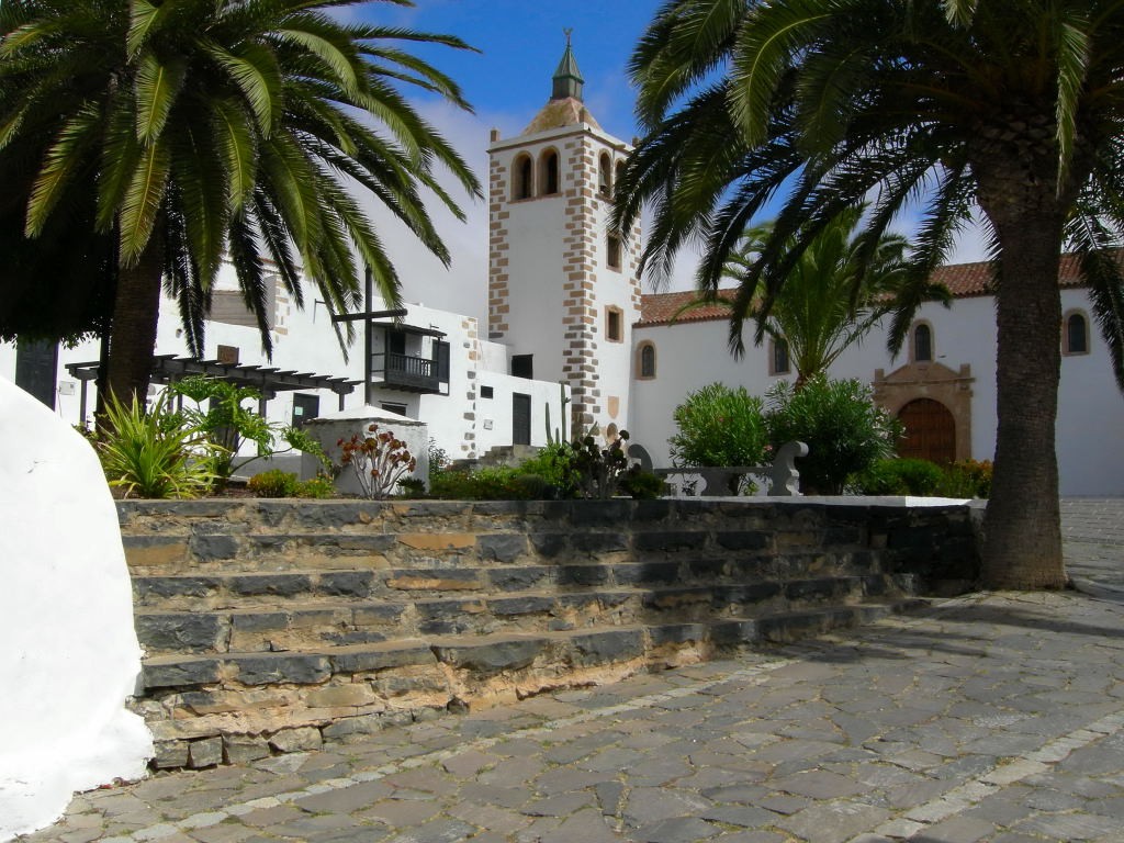 Historic white church in Betancuria, Fuerteventura, framed by palm trees and stone steps.
