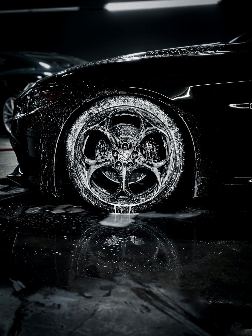Professional car detailing of a black luxury car with soapy foam on custom alloy wheels and tires.