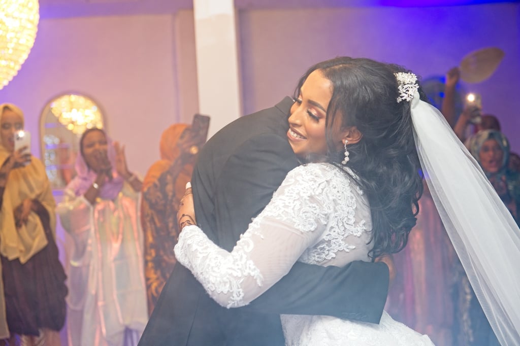 bride in white wedding dress hugging groom in black suit, purple mood lighting in blurry background