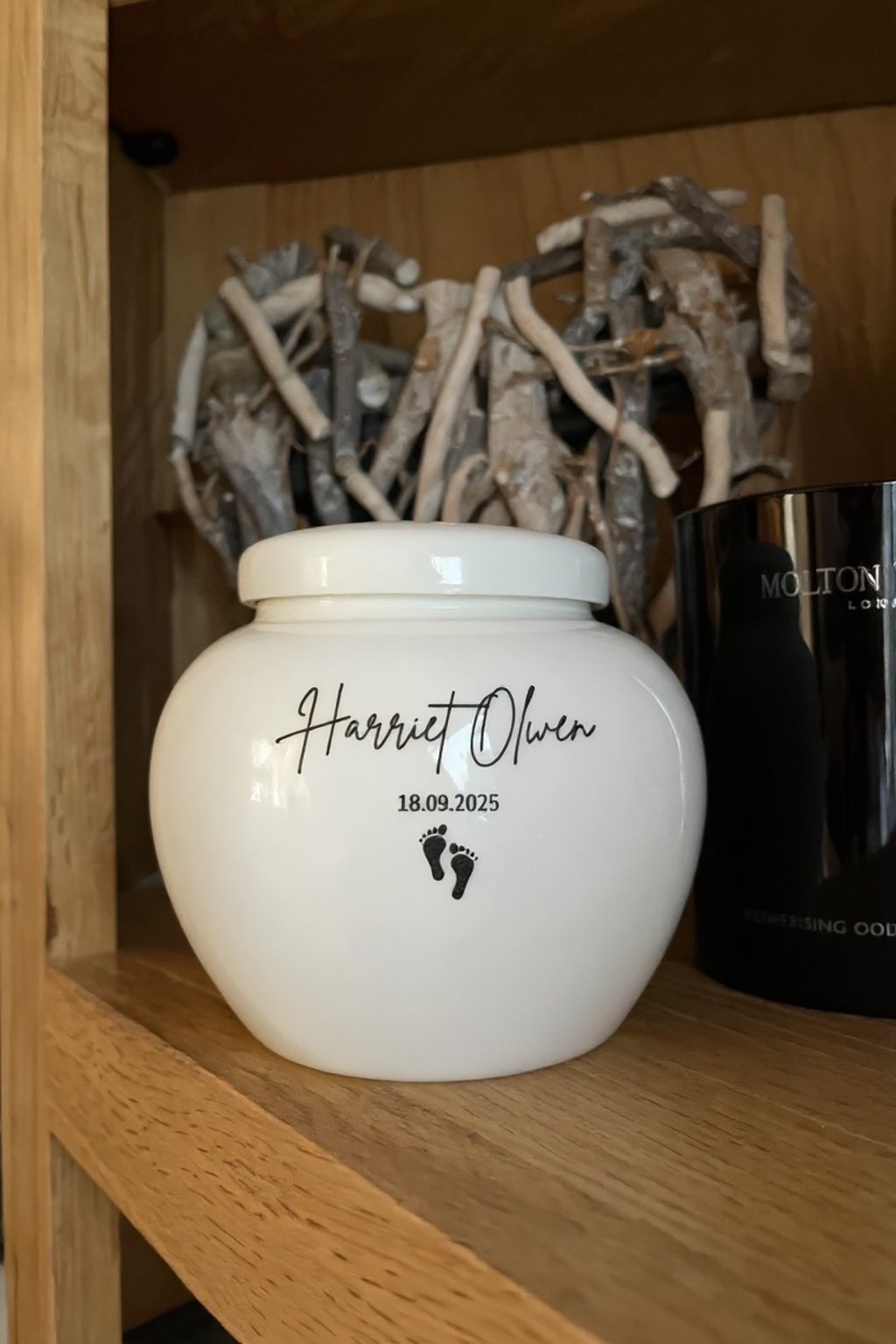 White ceramic baby memorial urn with calm rounded form, scripted ‘Harriet Olwen,’ date and tiny foot