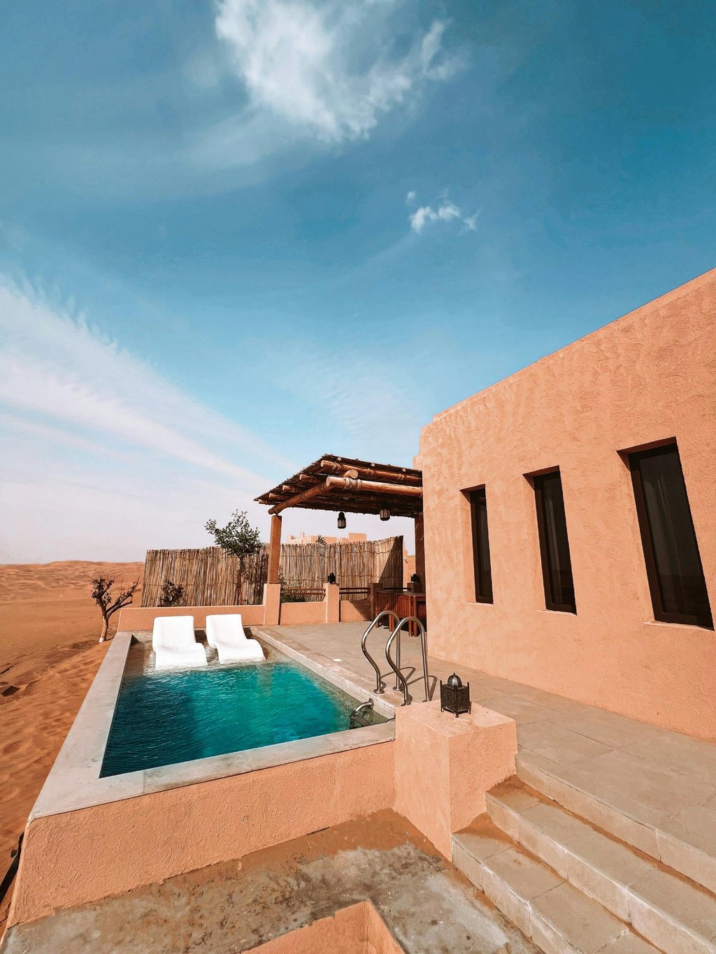 Luxury desert resort villa with a private infinity pool and sun loungers overlooking sand dunes.