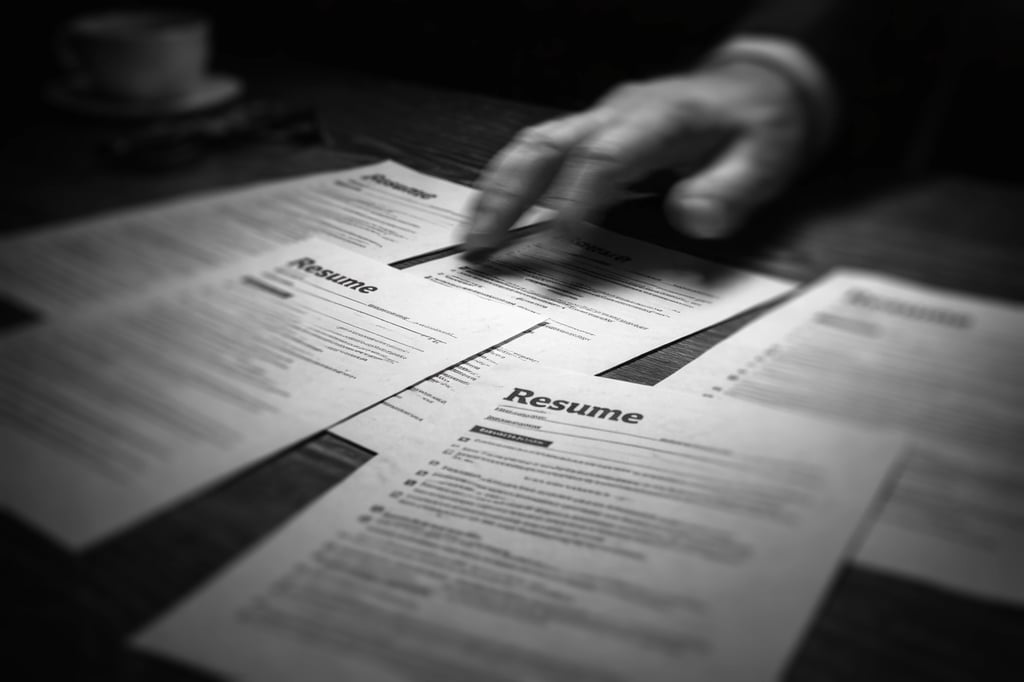 a hand rushing through several resumes spread across a table top