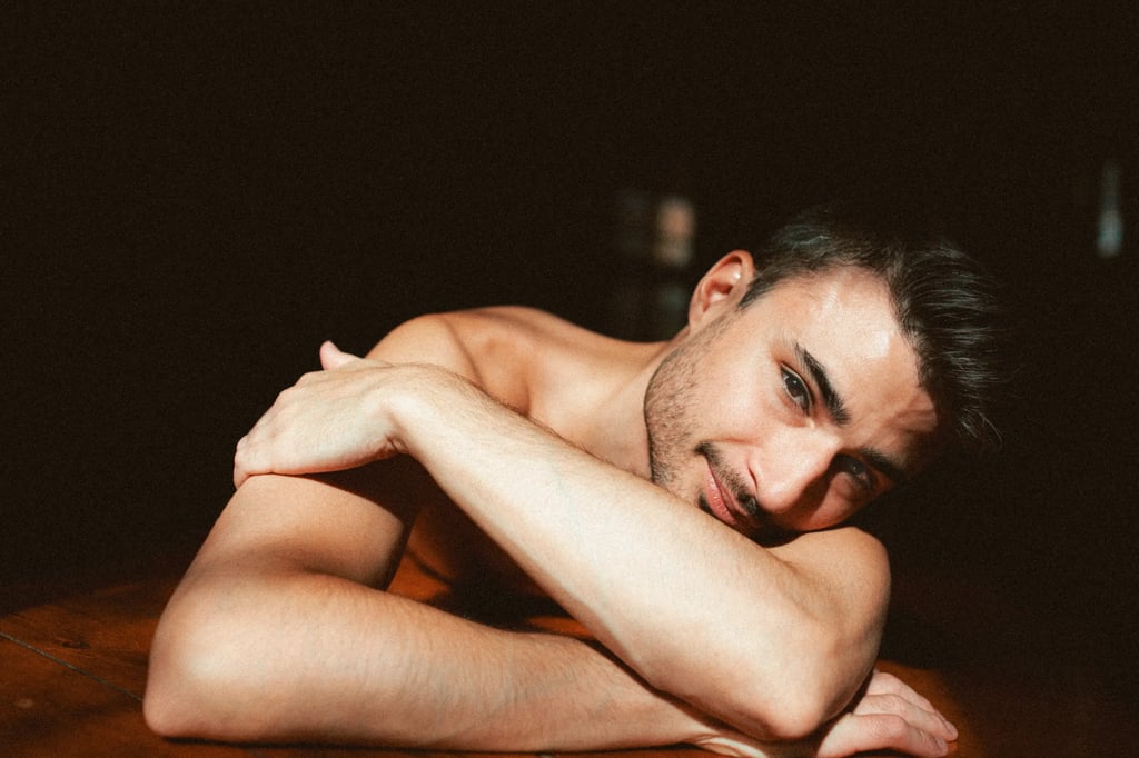 Photo boudoir homme nu en studio, lumière tamisée — Belle Tronche Montréal - Homme allongé, bras croisés, regard célin
