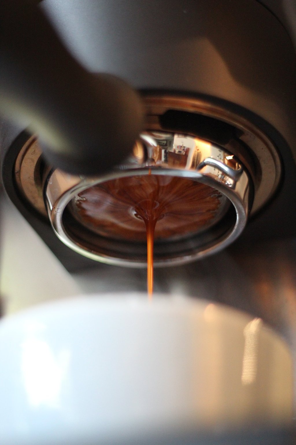 Fresh espresso shot pouring from a bottomless portafilter into a white ceramic cup.