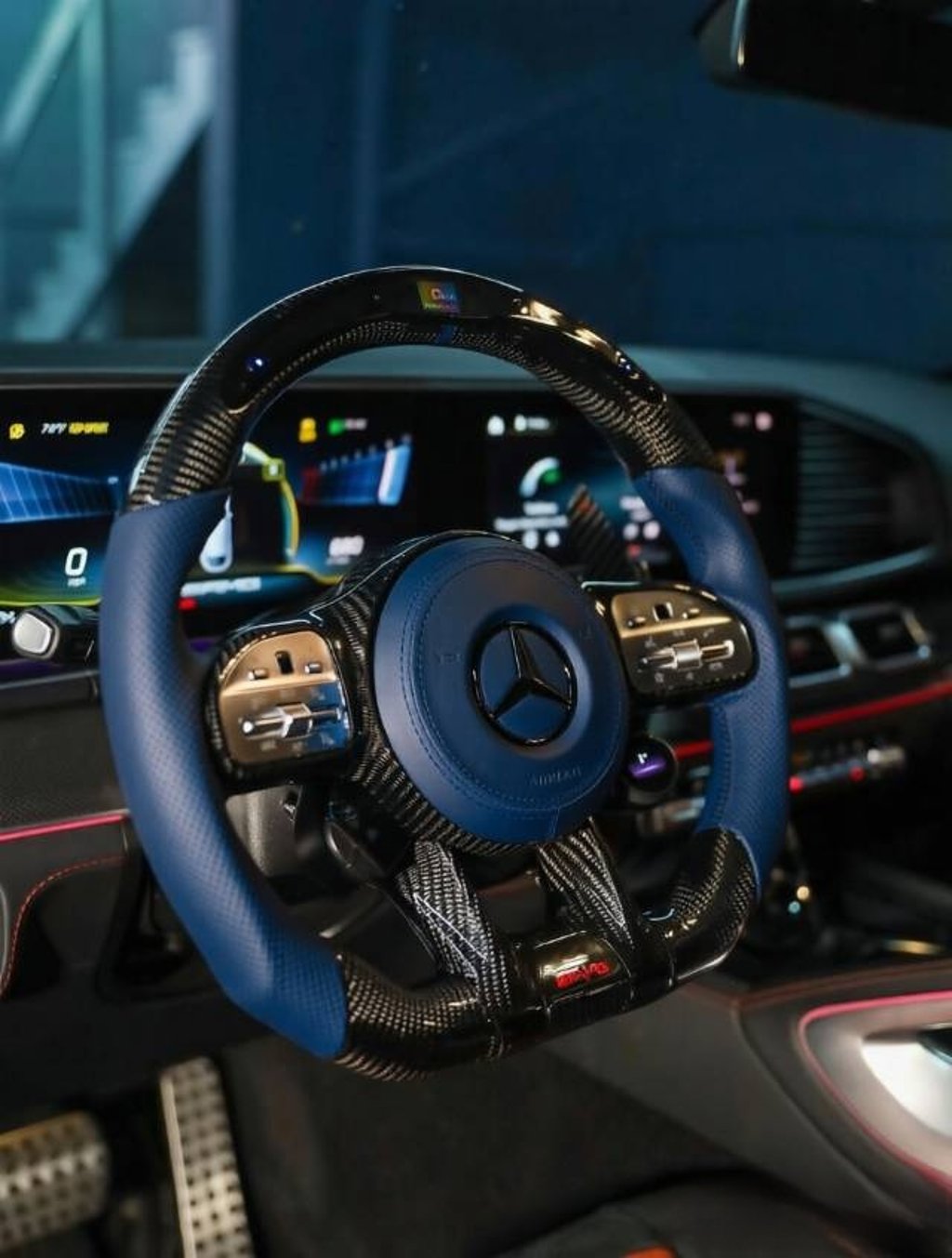 Custom blue and carbon fiber Mercedes AMG steering wheel inside a luxury car interior.