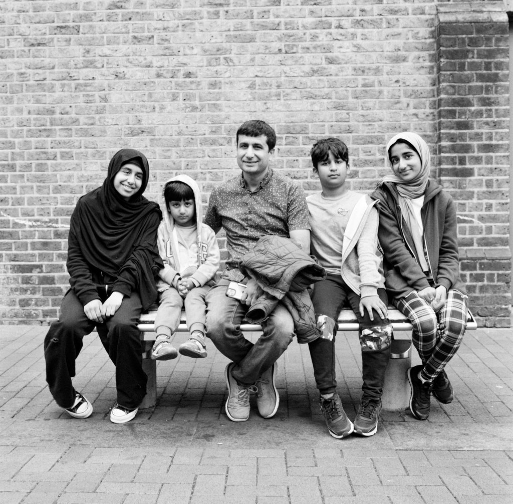 Muslim father and his children sitting on a bench in London