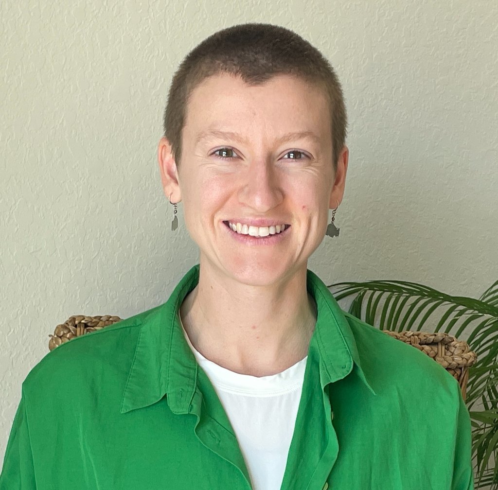 Smiling woman with a buzz cut wearing a green button-down shirt and dangling earrings.