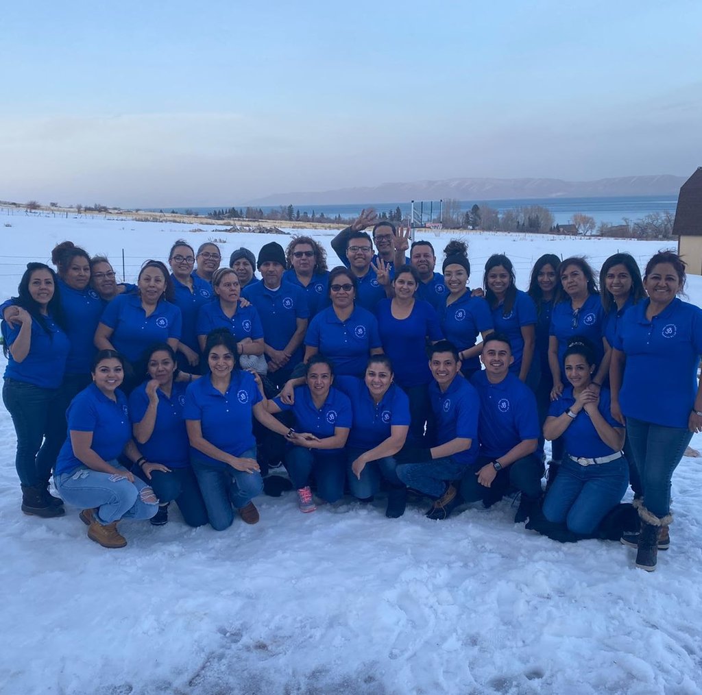 A large group of employees in blue polo shirts posing together in a snowy field with a lake view.