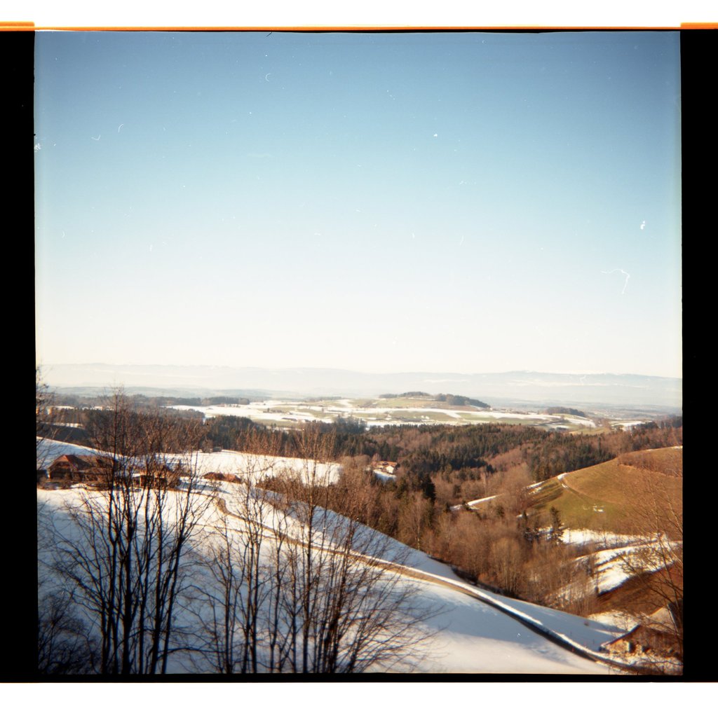 Blick auf sanfte Hügeln und verschneite Feldern unter strahlend blauem Himmel.