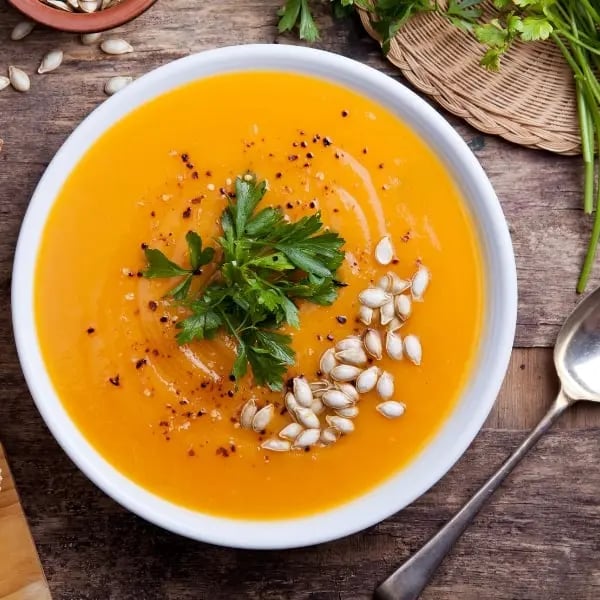 Une assiette de soupe au potiron, posé sur une vieille table en bois.