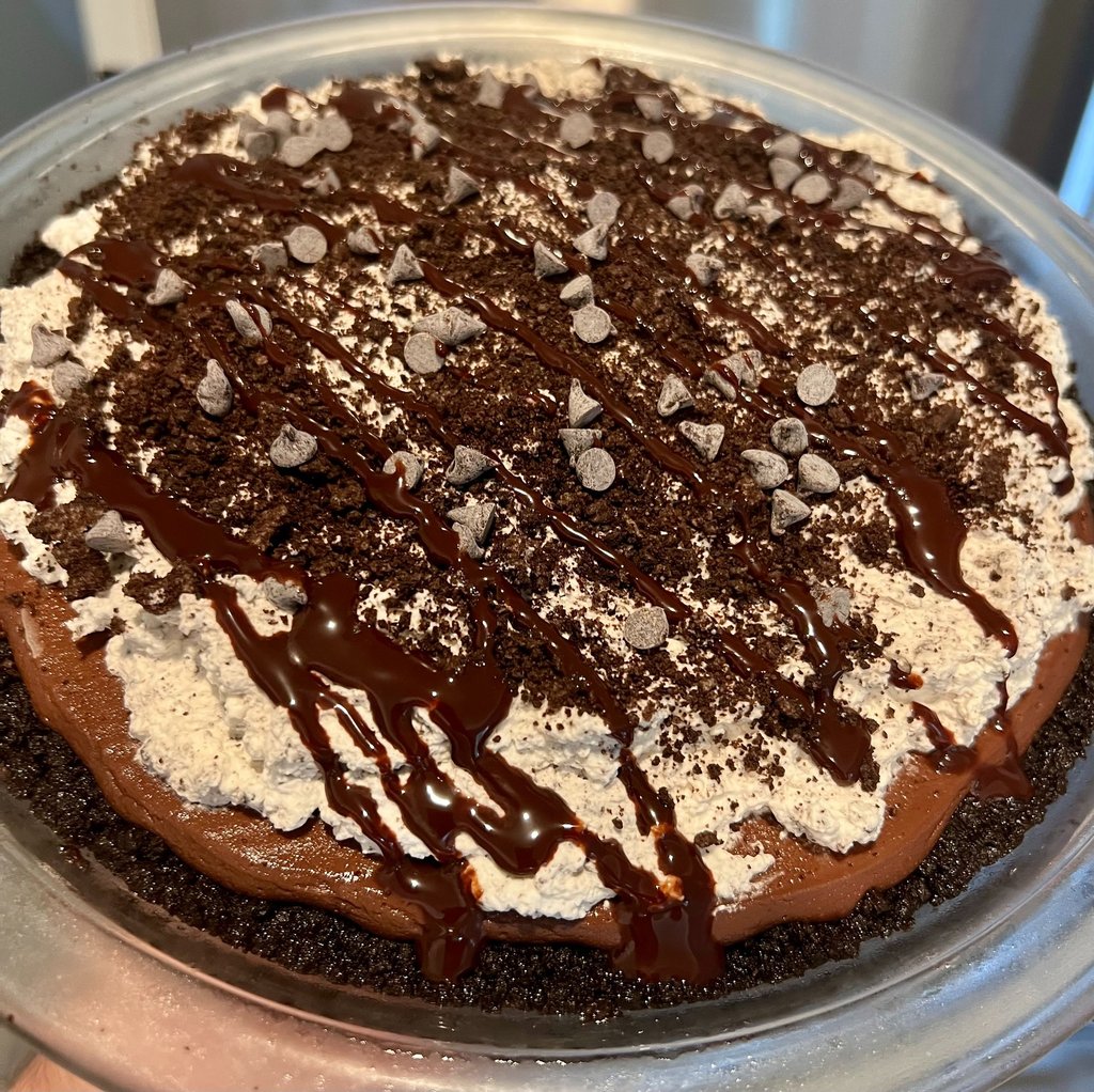 Chocolate silk pie with whipped cream, cookie crumbles, and chocolate drizzle in a glass dish.