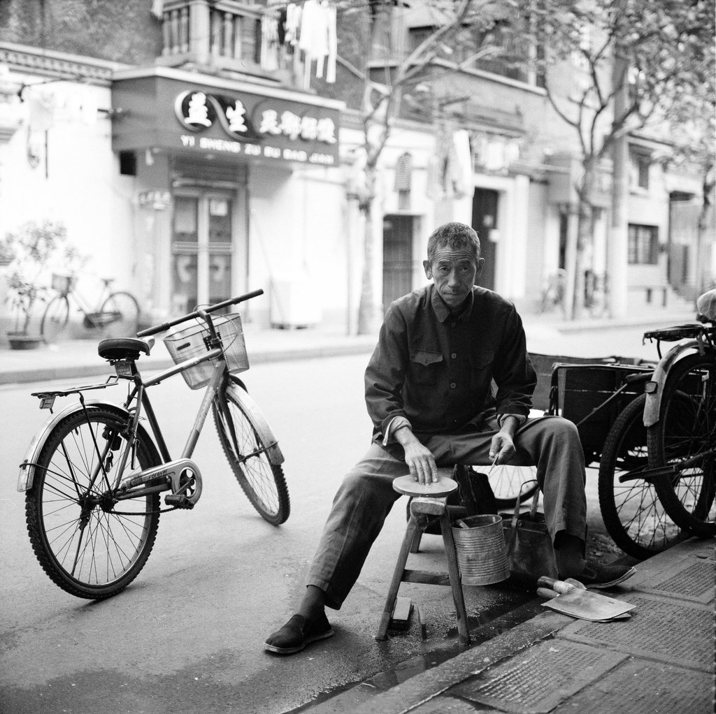 Man sits on a street in Shanghai sharpening his knives with a grindstone