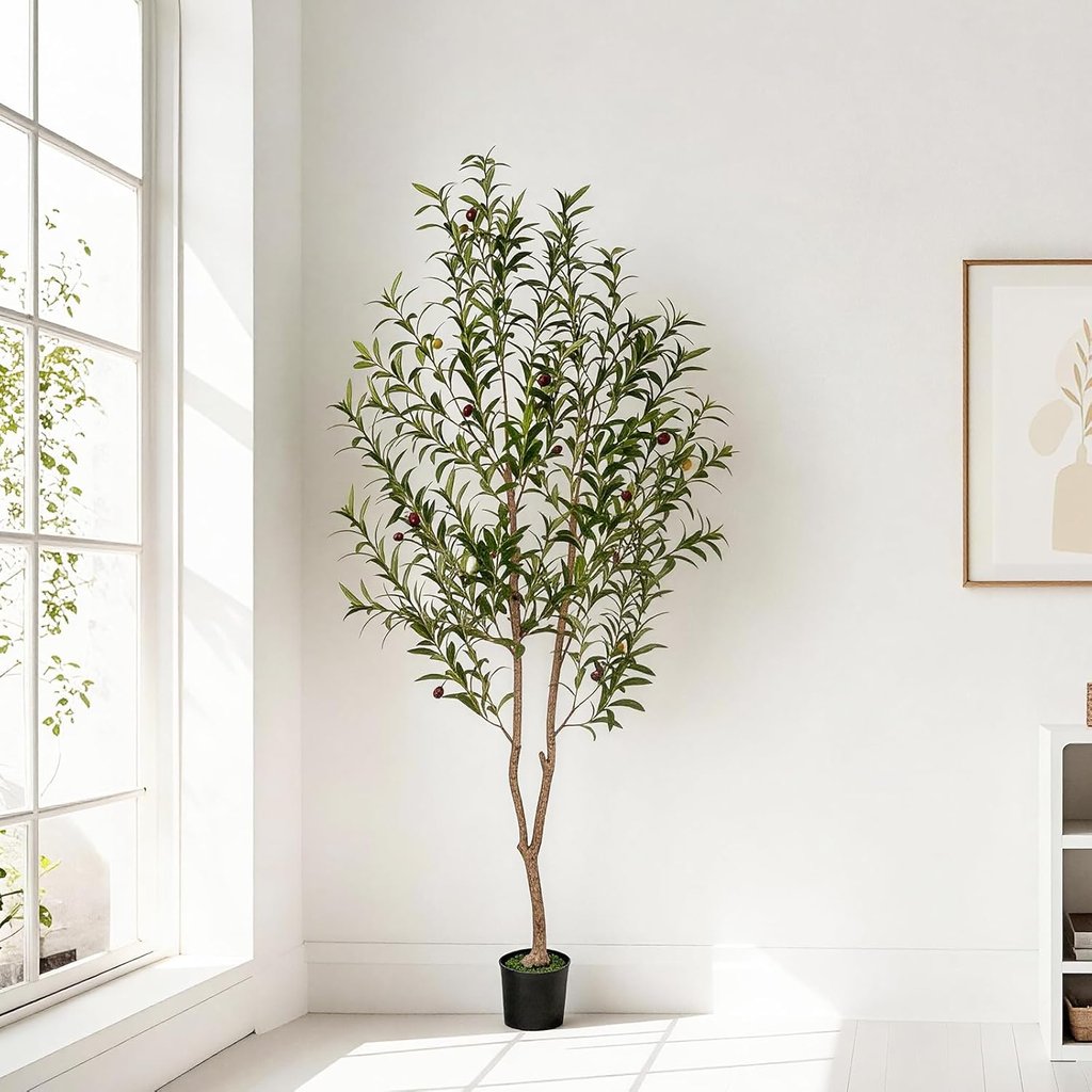Tall artificial olive tree in a black pot standing in a bright minimalist room with white walls.