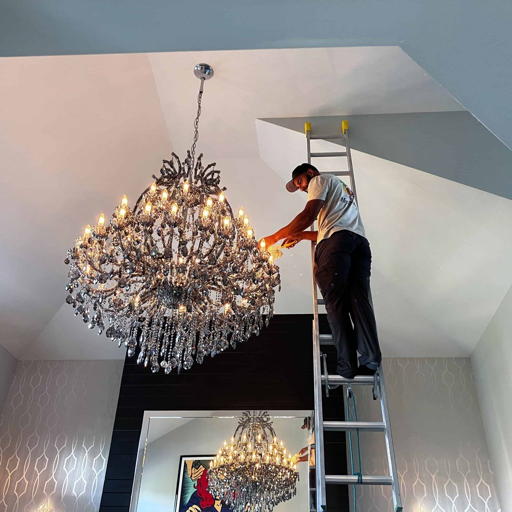 Mop Monkey technician dusting crystal chandelier from ladder in Calgary