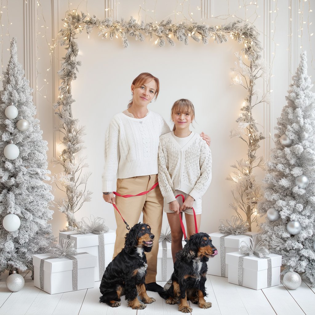 Mother and daughter posing with two spaniel dogs in a white winter holiday studio setting with lights.