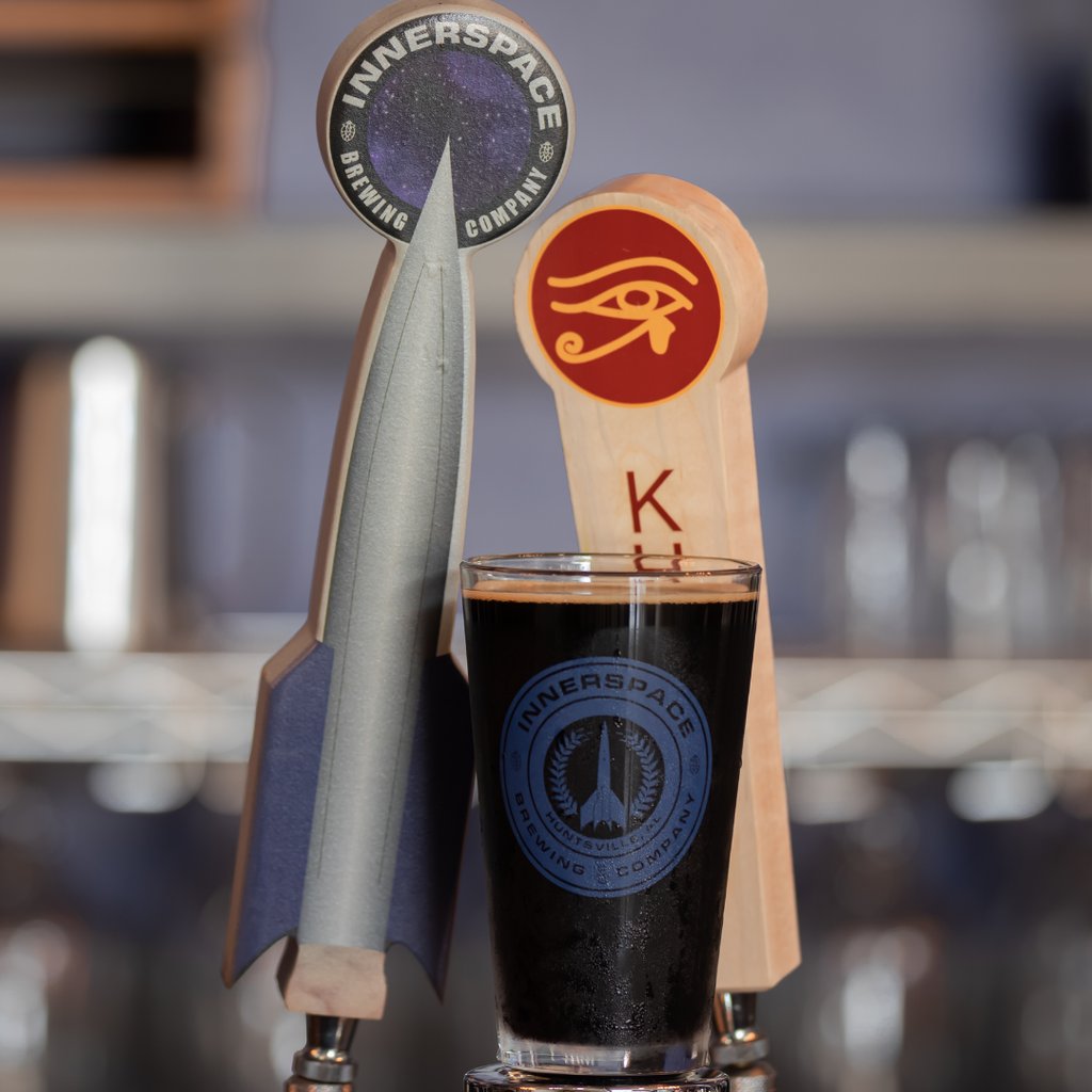 A pint of dark craft beer in an Innerspace Brewing Company glass next to a rocket-shaped tap handle.