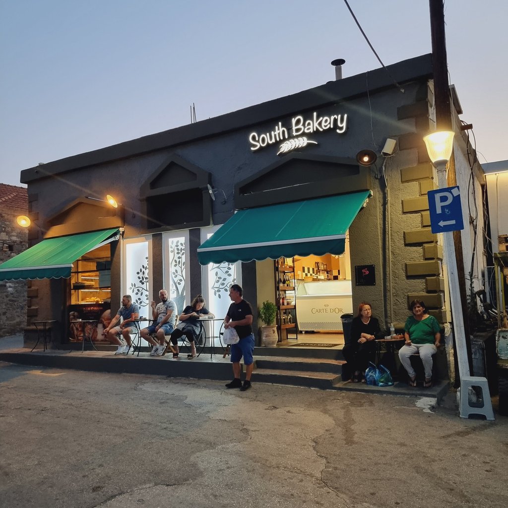 Customers sitting outside the South Bakery storefront with green awnings at dusk.